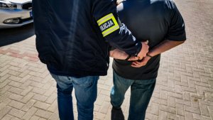 policjant kryminalny w cywilnych ubraniach prowadzi zatrzymanego 71latka