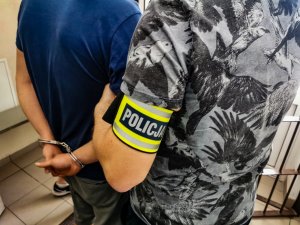 policjant kryminalny w cywilnych ubraniach trzyma za ramię zatrzymanego mężczyznę