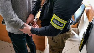 policjant kryminalny w cywilnych ubraniach, który zakłada kajdanki na ręce trzymane z tyłu