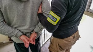 policjant kryminalny w cywilnych ubraniach, który trzyma mężczyznę z założonymi kajdankami