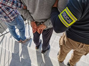 policjanci kryminalni w cywilnych ubraniach trzymają zatrzymanego mężczyznę z założonymi kajdankami
