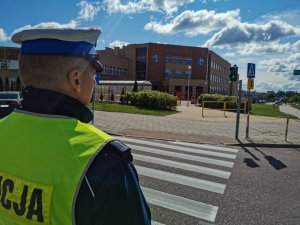 Policjant stojący przed szkołą obserwujący przejście dla pieszych