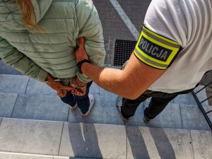 policjant kryminalny z opaską z napisem &quot;POLICJA&quot; trzyma zatrzymaną kobietę