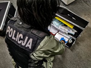 policjantka w cywilnych ubraniach z założoną czarna kamizelką z napisem &quot;POLICJA&quot;. Policjantka przegląda odzyskany sprzęt medyczny