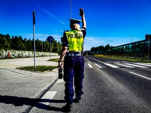 Policjantka z uniesioną ręką  zatrzymuje pojazd do kontroli