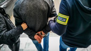 policjant kryminalny w cywilnych ubraniach trzymający zatrzymanego mężczyznę