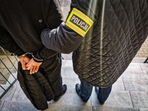 policjant kryminalny w cywilnych ubraniach trzymający zatrzymanego mężczyznę