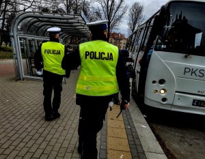 Dwóch policjantów idących w kierunku autobusu komunikacji publicznej.