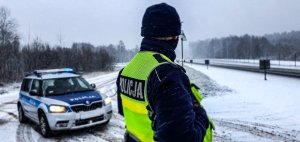 Policjant stojący przy jezdni obok radiowozu, w tle padający śnieg