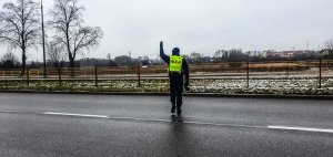 Policjant z podniesioną ręką zatrzymujący pojazd do kontroli.