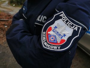 Ramię policjanta, na nim naszywka z napisem Policja, dzielnicowi.