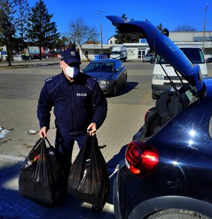 Policjant stojący z reklamówkami w ręku przy samochodzie