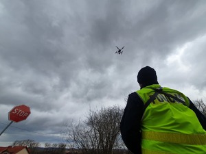 Policjant obsługujący drona, w tle lecący dron.