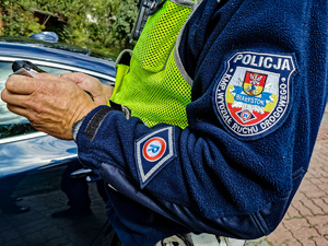 Policjant z drogówki trzymający w ręku dokument i sprawdzający w urządzeniu osobę
