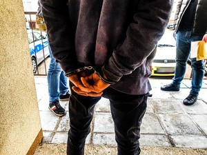 Zatrzymany mężczyzna z założonymi kajdankami, obok dwóch policjantów.