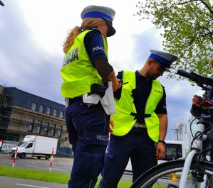 Policjanci stojący bokiem kontrolujący rowerzystkę