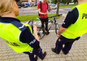 Policjanci stojący tyłem, kontrolujący rowerzystę