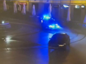 Zdjęcie nagrania z monitoringu. Samochód osobowy jadący bez świateł, za nim jadący radiowóz policyjny.