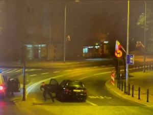 Zdjęcie z nagrania z monitoringu. Mężczyzna wybiegający z samochodu osobowego i wybiegający policjant z radiowozu.