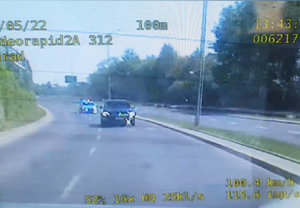 Ujęcie nagrania z tylnej kamery radiowozu - pojazd osobowy jadący jezdnią, za nim radiowóz na sygnałach.