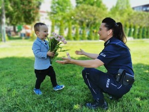 Policjantka z wyciągniętymi rękoma, obok idące w jej kierunku dziecko z kwiatami.