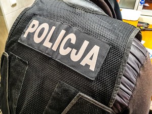 Plecy policjanta w kamizelce z napisem policja.