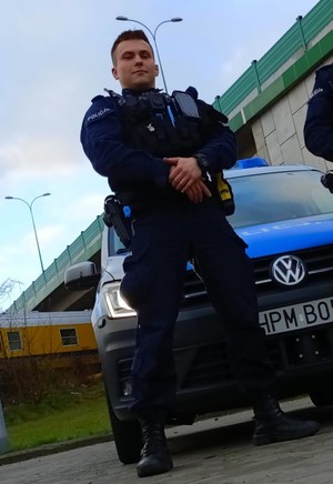 Umundurowany policjant stojący na tle radiowozu