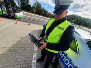 Policjant przy radiowozie obsługujący dron.