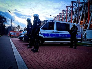 Policjanci stoją przy radiowozach, w tle stadion