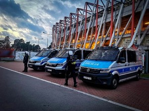 radiowozy zaparkowane przy stadionie, obok policjanci