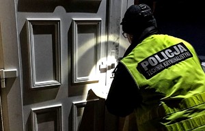 Policjant przy drzwiach do altanki w kamizelce z napisem technik kryminalistyki