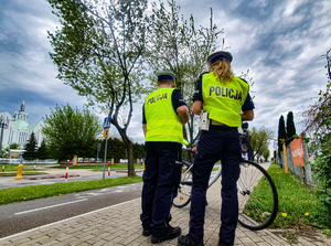 Dwoje policjantów stojących tyłem, kontrolujących rowerzystę