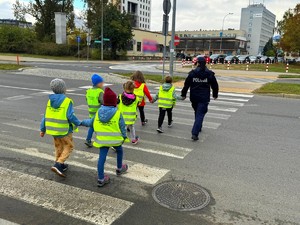 Policjantki w terenie z przedszkolakami ćwiczą przechodzenie przez przejście dla pieszych.