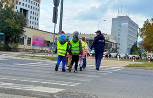 Policjantki w terenie z przedszkolakami ćwiczą przechodzenie przez przejście dla pieszych.