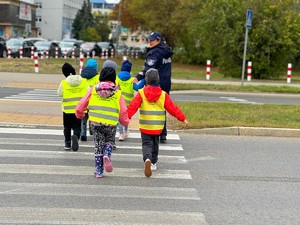 Policjantki w terenie z przedszkolakami ćwiczą przechodzenie przez przejście dla pieszych.