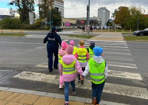 Policjantki w terenie z przedszkolakami ćwiczą przechodzenie przez przejście dla pieszych.