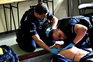 dwóch policjantów pochylonych nad fantomem udzielających pierwszej pomocy przedmedycznej