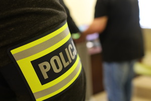 opaska policjanta, w tle zatrzymany mężczyzna