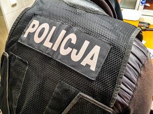 Policjant stojący tyłem w kamizelce z napisem policja.